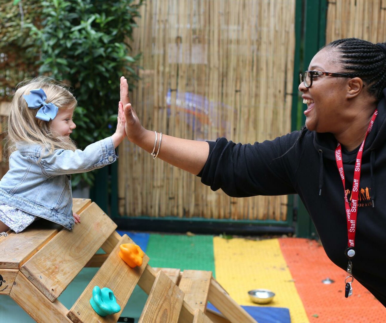 Nursery teacher and child do a high five in the playground