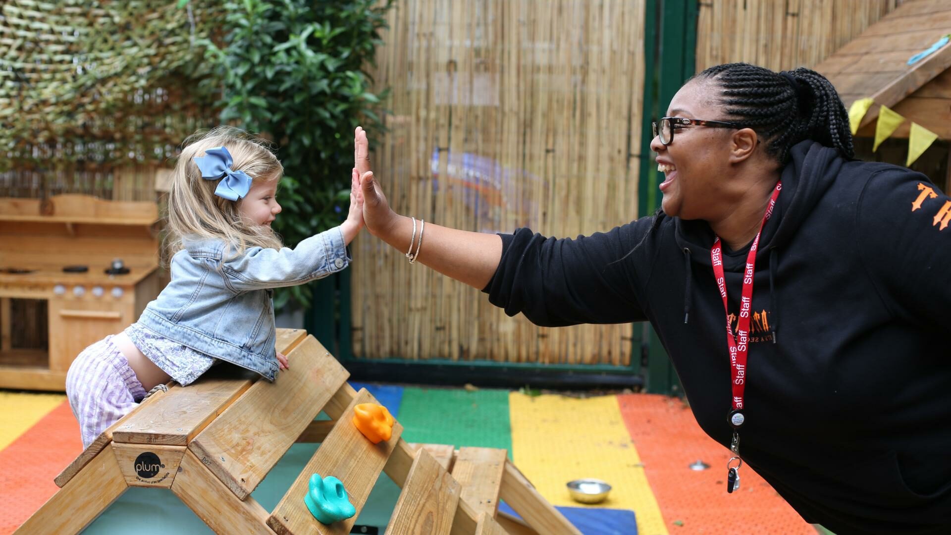 Nursery teacher and child do a high five in the playground