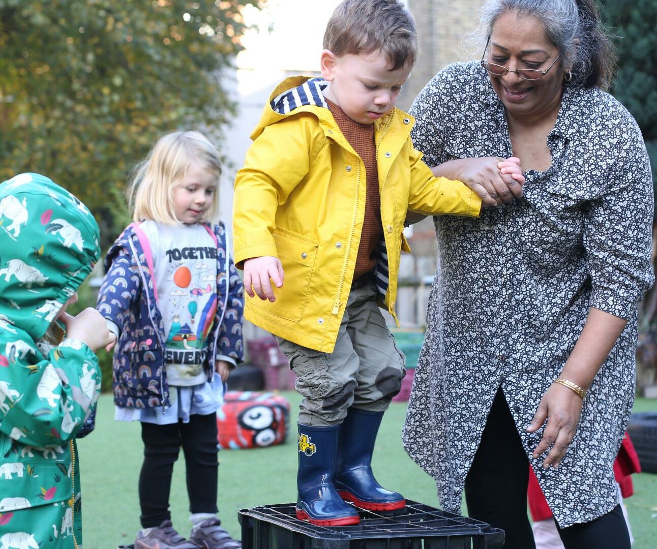 Staff and child outside in the garden practicing risky play and jumping off some crates.