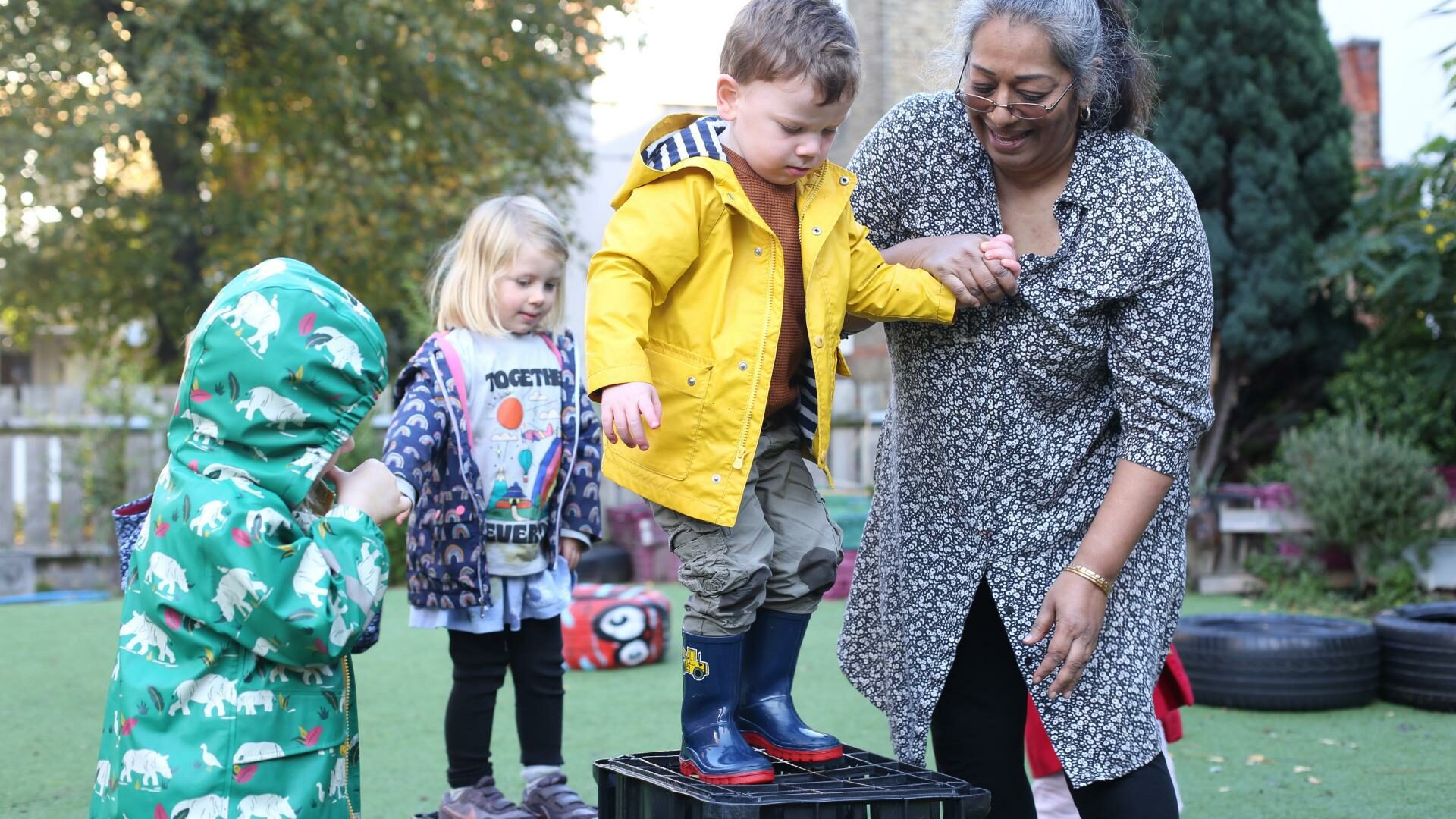 Staff and child outside in the garden practicing risky play and jumping off some crates.