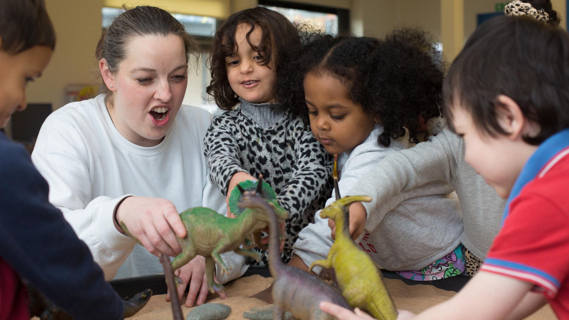 staff and children playing with sand and dinosaurs