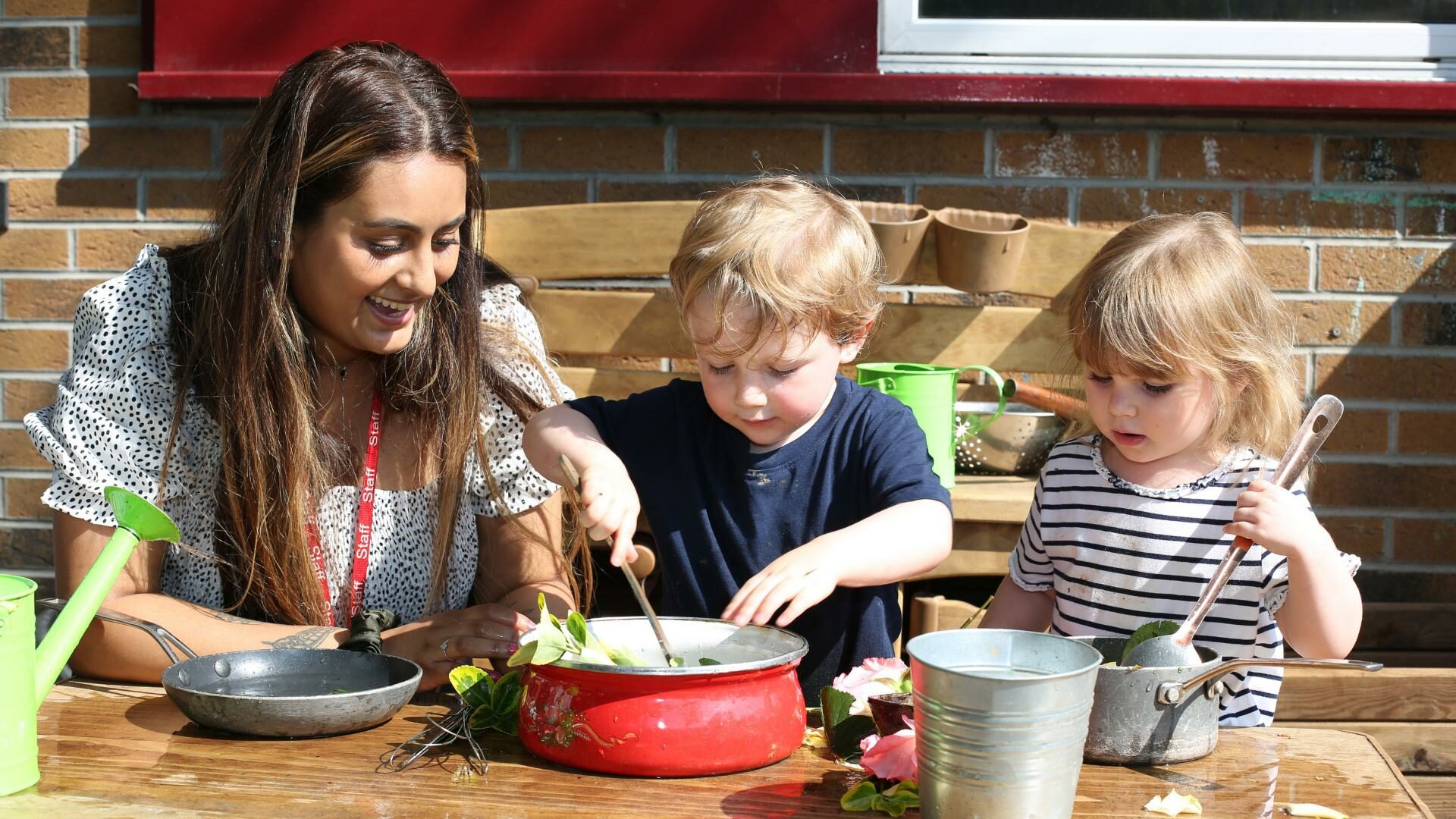 staff and children playing in the outdoor home corner using