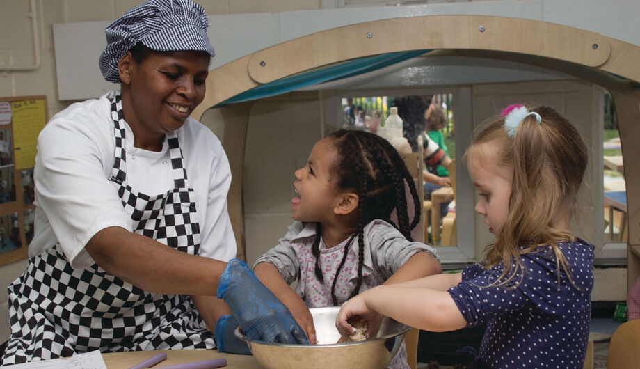 Children mixing dough in a bowl with the chefs help