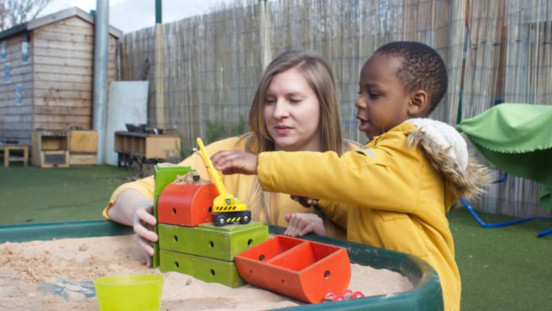 Staff and child playing outside with sand and blocks