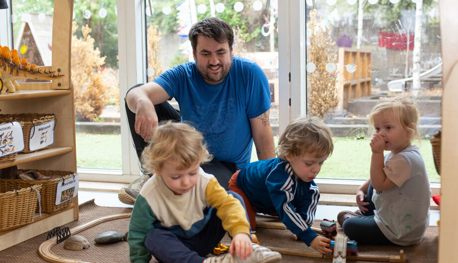 Children playing with train set with male teacher looking on
