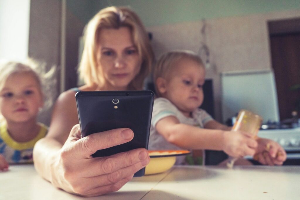 Mother looking at phone while holding children at the table 
