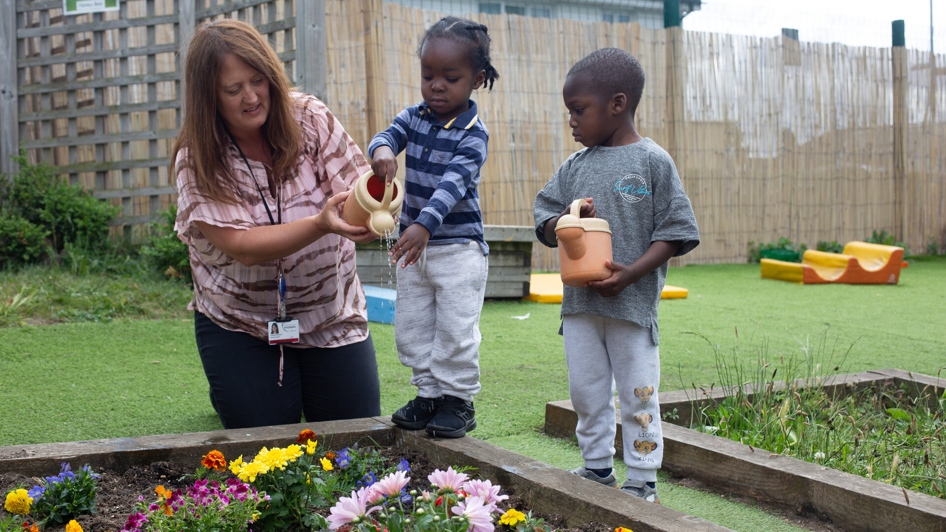 Children watering flowers with the help of a staff member