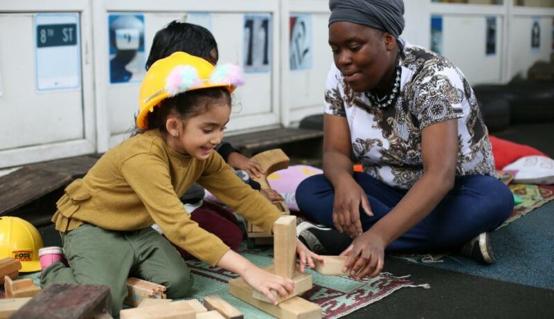 Child in a toy hard hat playing with blocks with a staff member