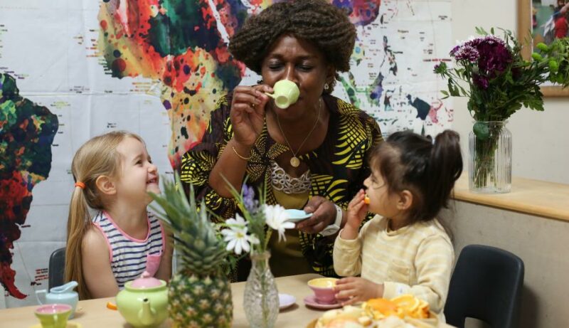 Staff member drinking a pretend cup of tea with two children