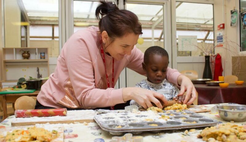 Staff member helping a child roll out dough