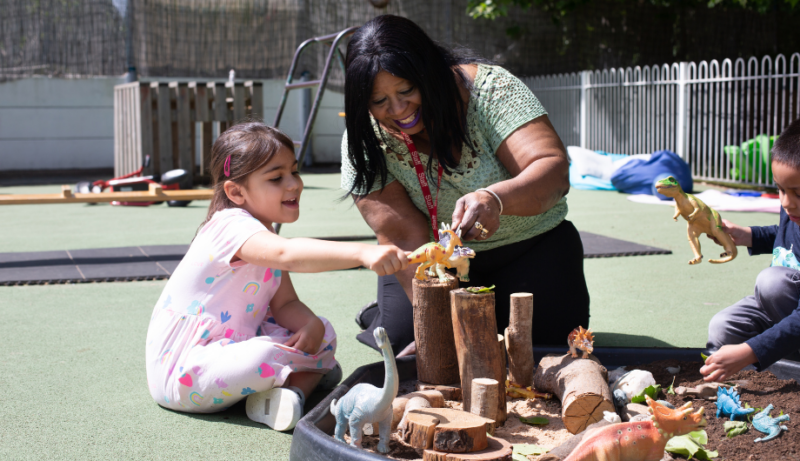 Staff member and child playing with toy dinosaurs
