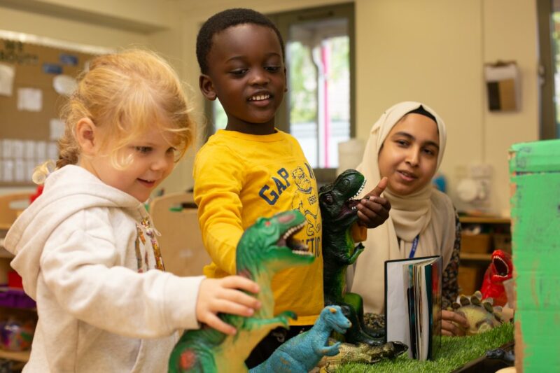 Children playing with dinosaurs in their teacher presence.